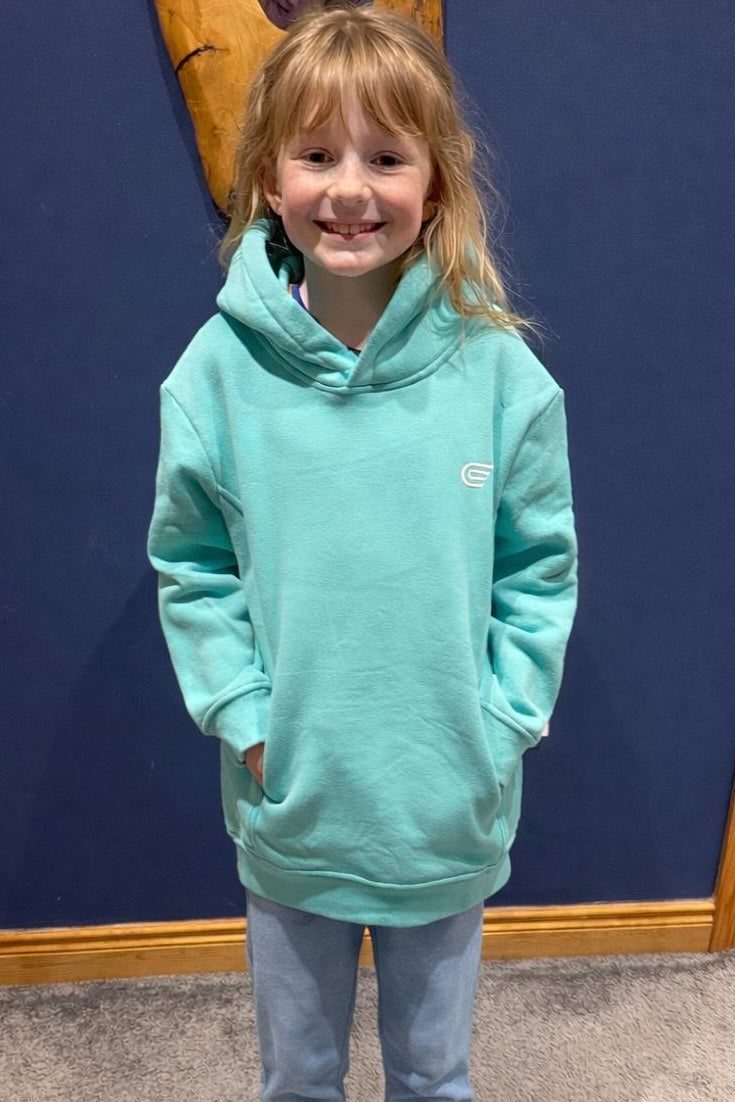 Child wearing a light blue hoodie and jeans standing in front of a blue wall.