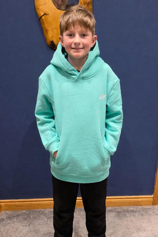 Child wearing a teal hoodie standing in a room with a blue wall and wooden door.